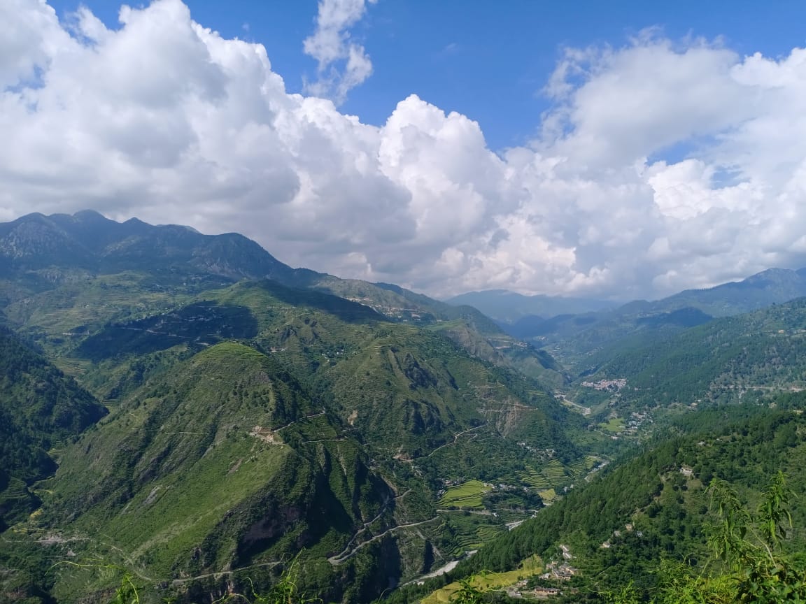 Wide landscape view of green mountain valleys and ridges under a blue sky with large white clouds