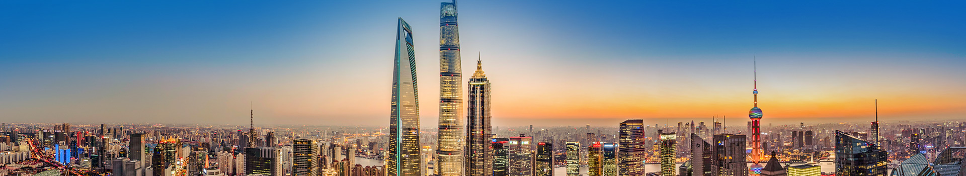 Panoramic city skyline at dusk with illuminated skyscrapers and a colorful sunset sky